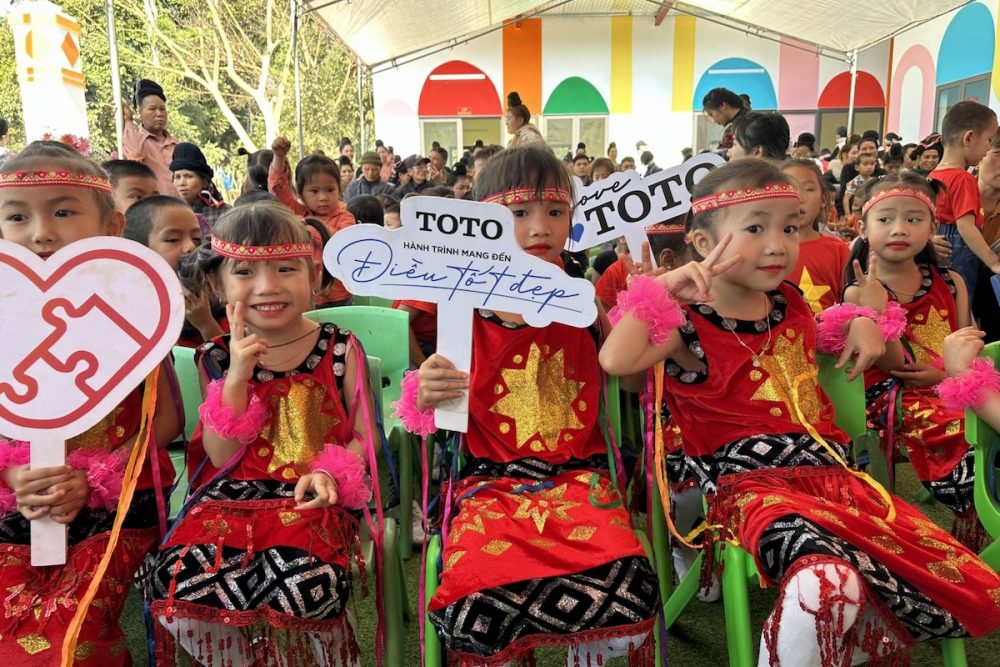 Happy children sit with smiles on their faces holding signs at the opening of a new school building in 2023, the 14th school built in Na Pan village, northwest of Hanoi by TOTO
