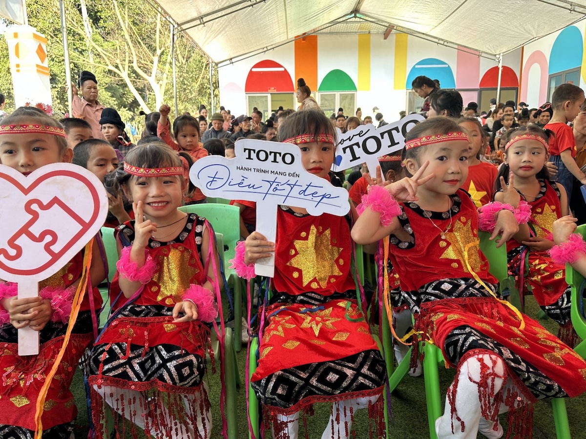 Happy children sit with smiles on their faces holding signs at the opening of a new school building in 2023, the 14th school built in Na Pan village, northwest of Hanoi by TOTO